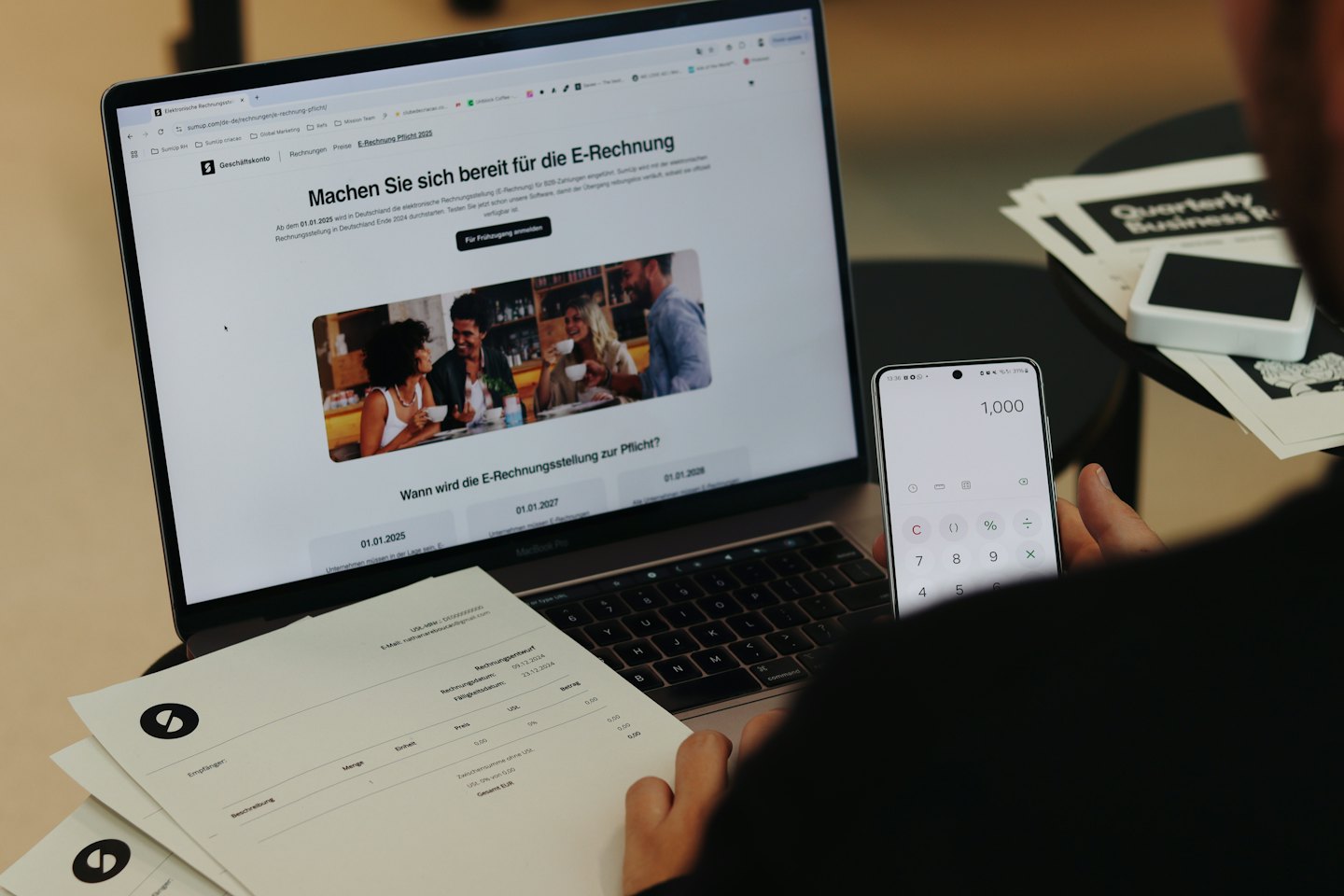 Hands hold a smartphone showing a calculator next to business reports.