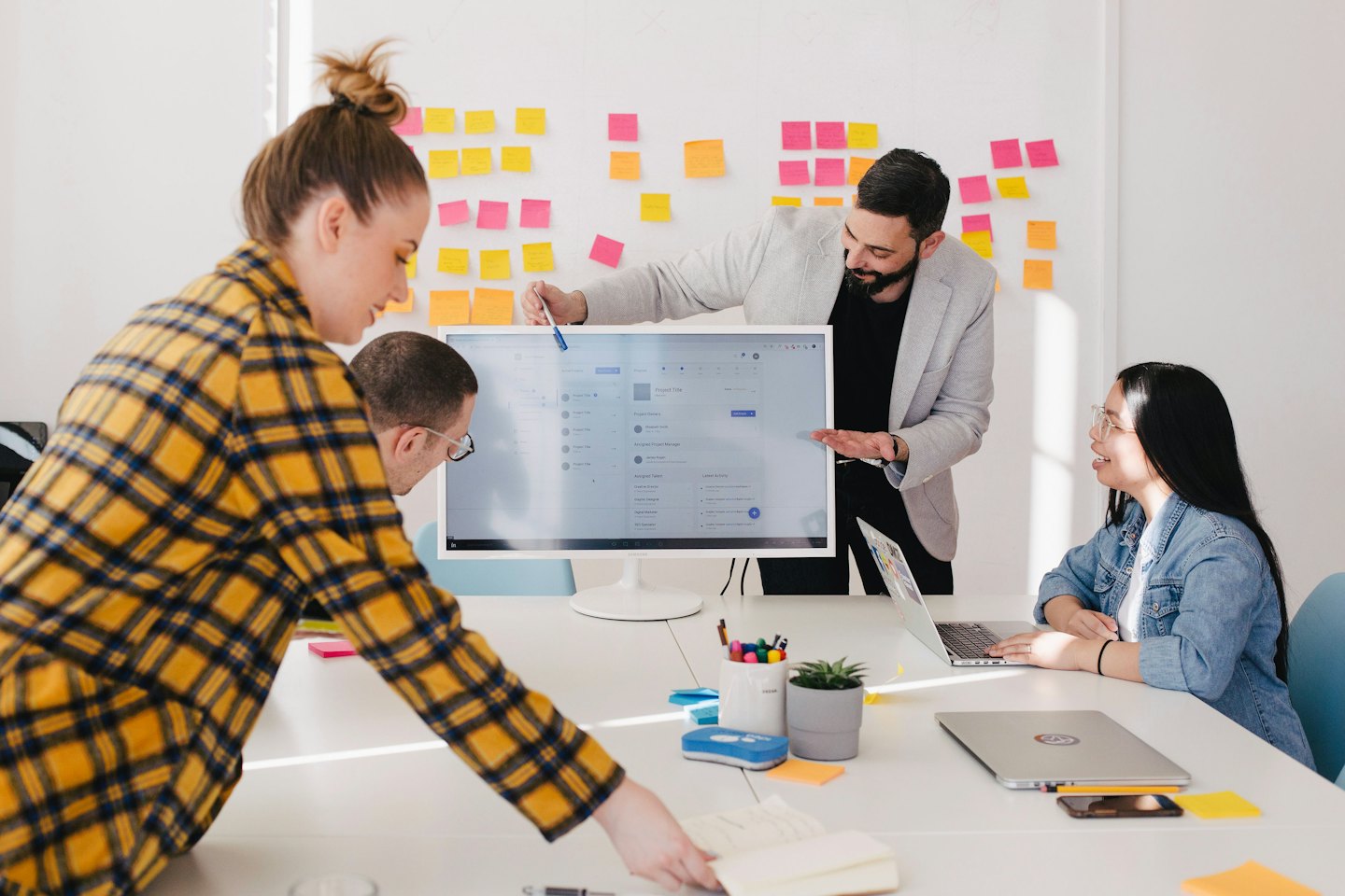 Four professionals collaborate around a monitor in a modern office.