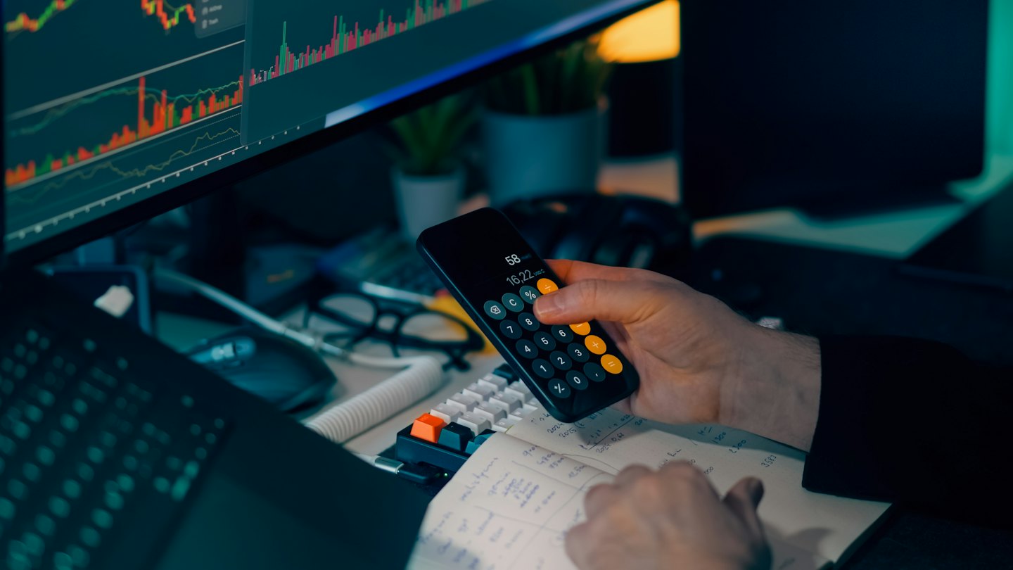 Hands using a smartphone calculator over financial notebook.