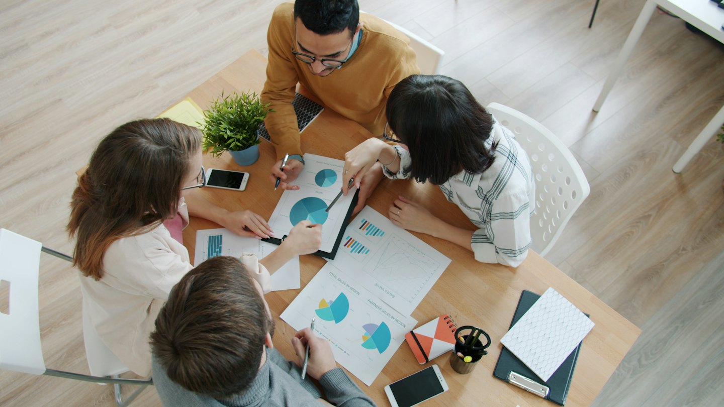 Diverse team collaborates over business charts at a light wood table.