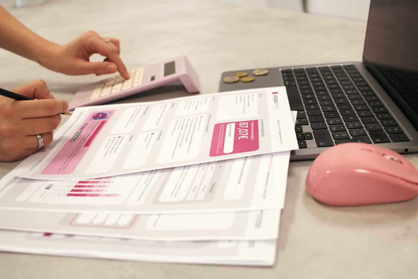 Person reviewing financial documents with a pink calculator and laptop.