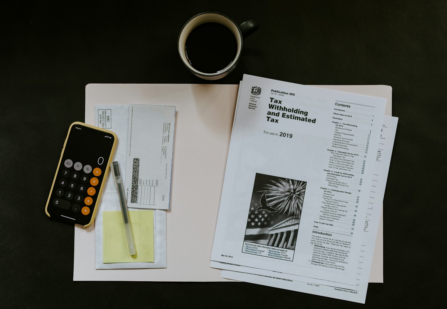 Desk with tax forms, coffee, and phone for tax preparation.